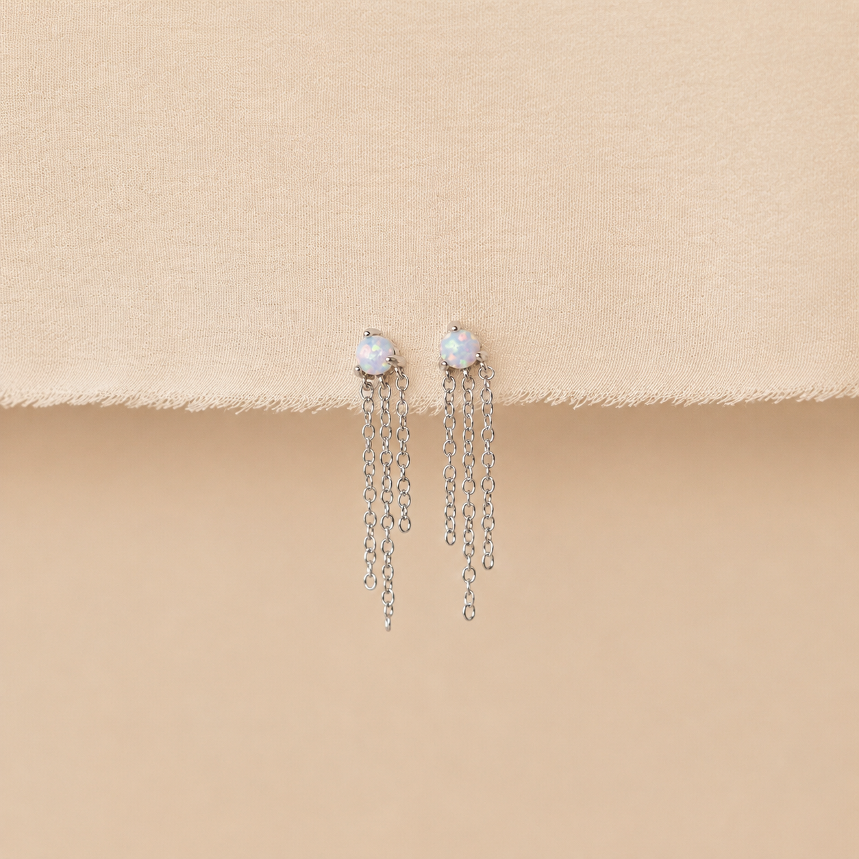 Pair of earrings with pearl-like stones and chain drops on a beige surface